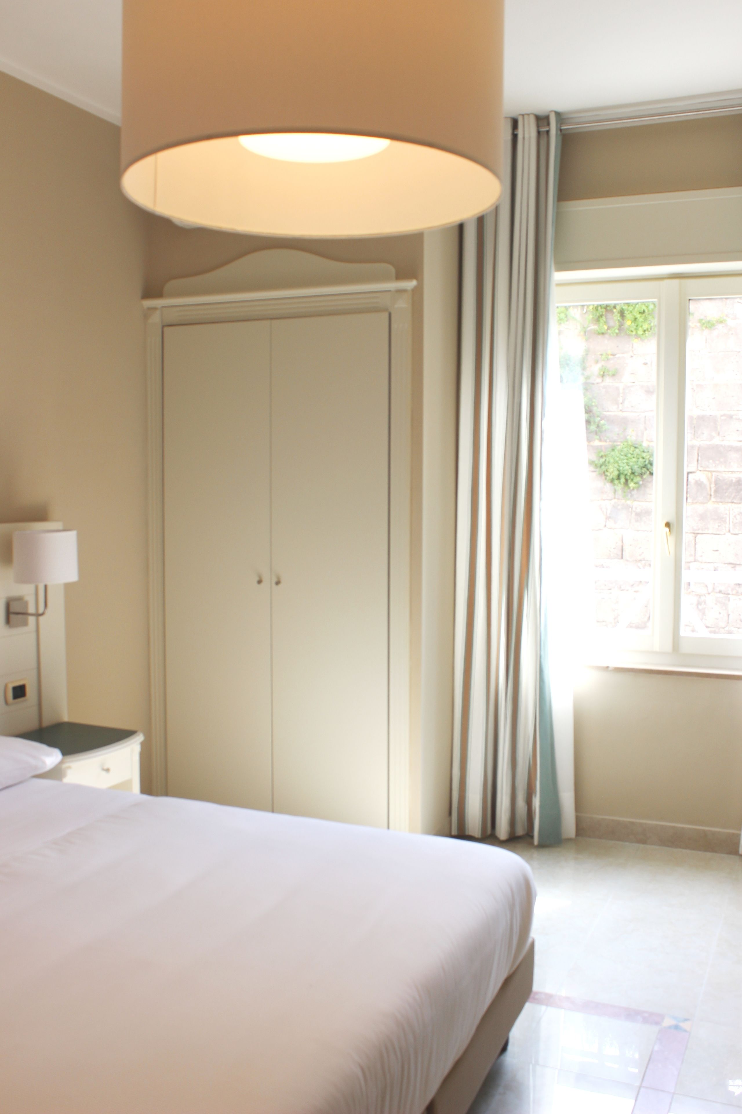 Une chambre à coucher comprenant un lit, une armoire, une table de chevet, une lampe et une fenêtre avec des rideaux.