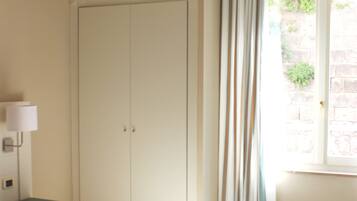 Une chambre à coucher comprenant un lit, une armoire, une table de chevet, une lampe et une fenêtre avec des rideaux.
