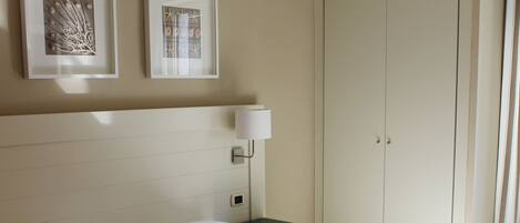 A neatly made bed with white linens, a bedside table with a lamp, and two framed artworks on the wall.