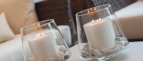 Two glass candle holders with white candles and pebbles on a wooden table.