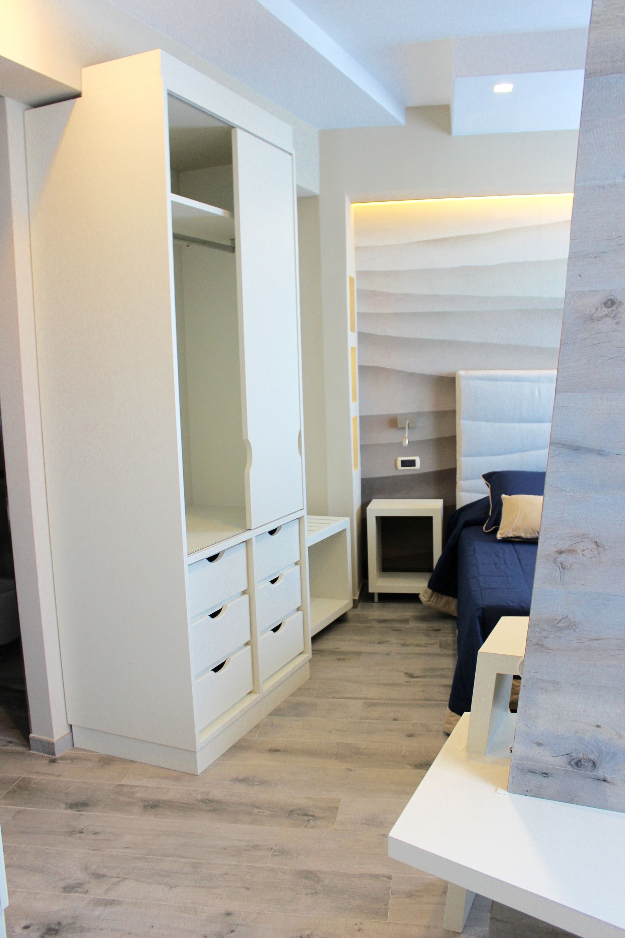 A bedroom with a white wardrobe, a bedside table, and a bed with a headboard.