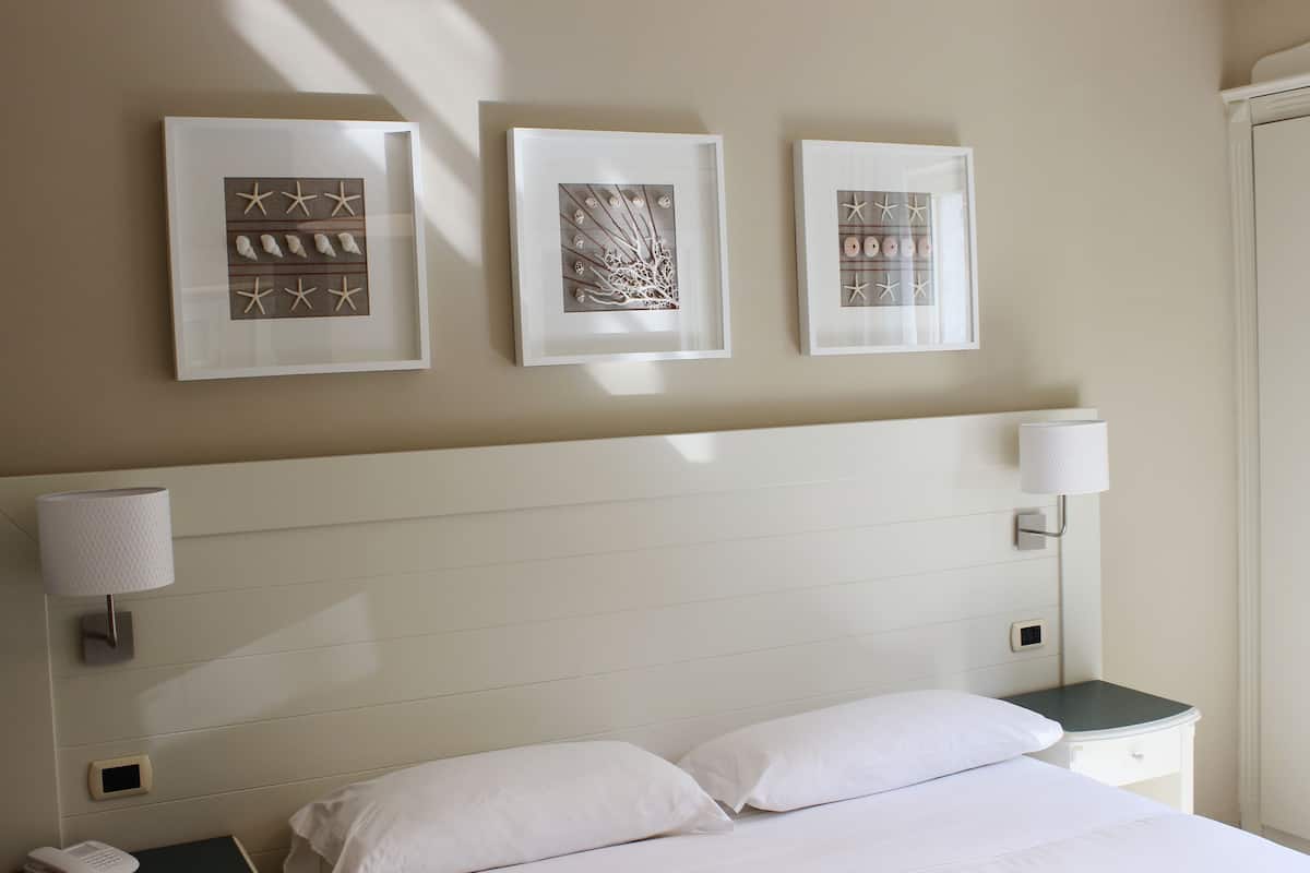 A hotel room with a bed, two bedside lamps, a nightstand, and three framed artworks on the wall.