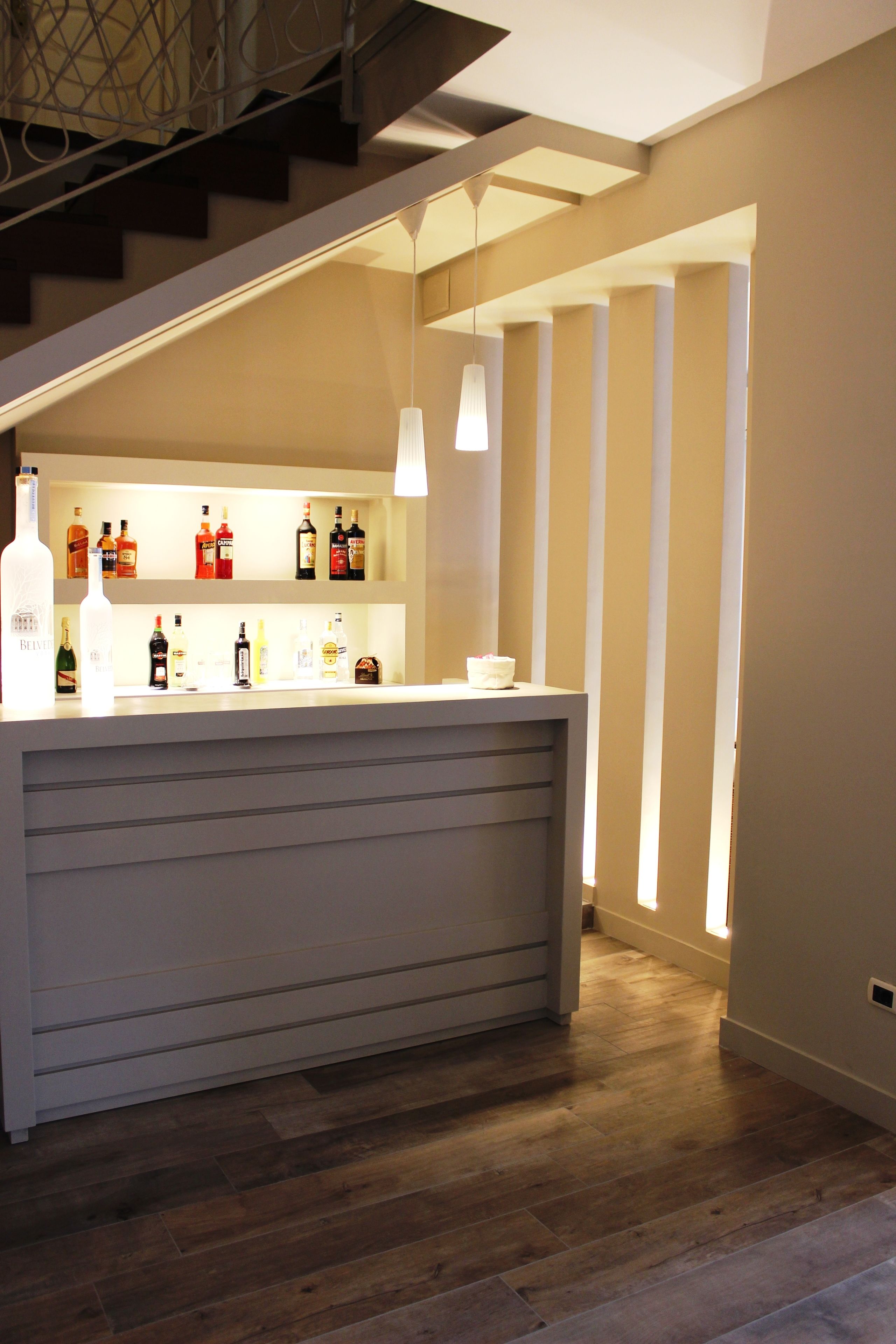 Eine Bar mit Theke und Regalen voller Flaschen, einer Treppe und einer Pendelleuchte.