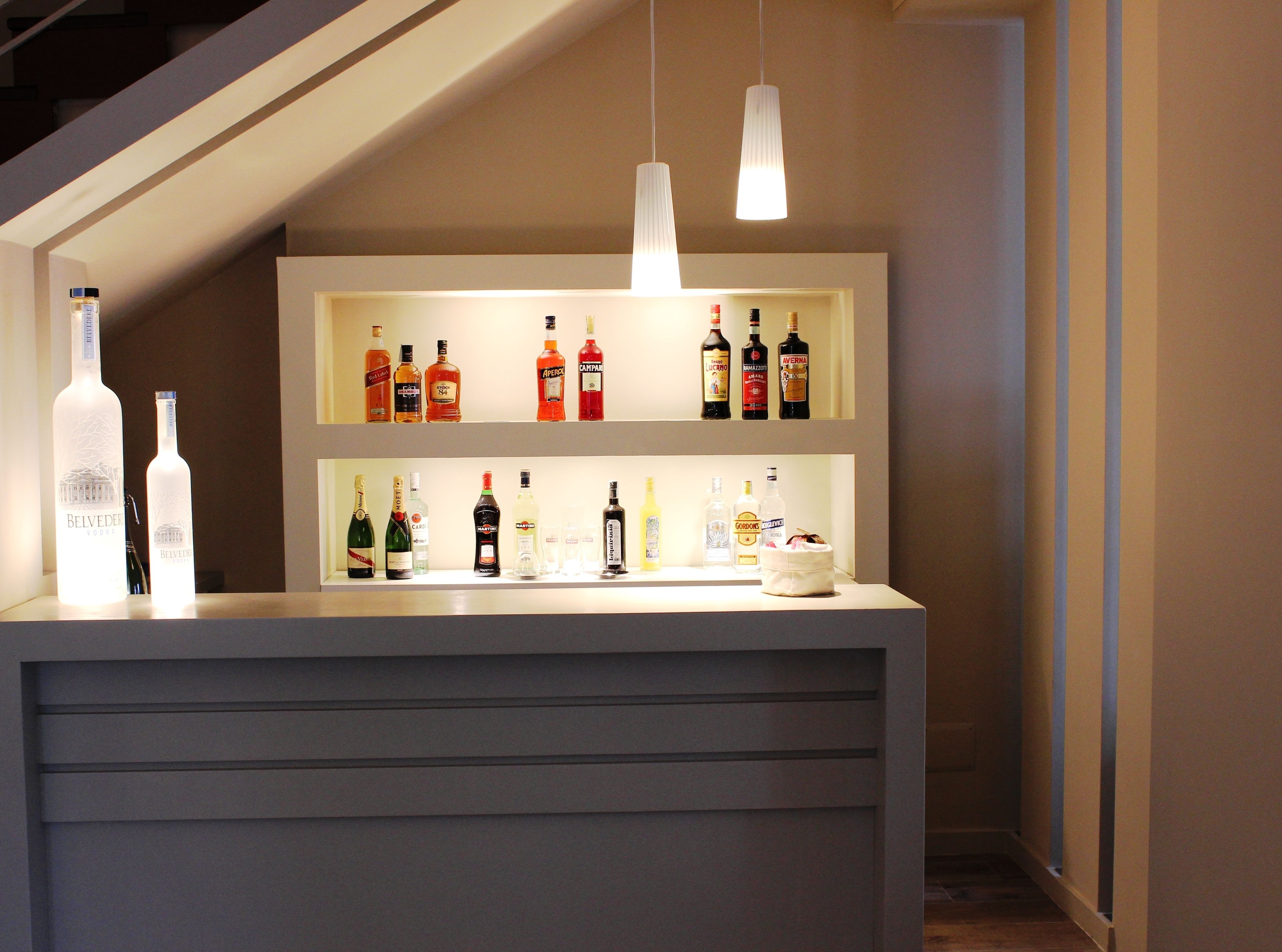 A bar area with shelves of liquor bottles, a white counter, and pendant lighting.