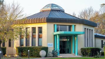 A modern building with a dome-shaped roof, large windows, and a teal-colored entrance.