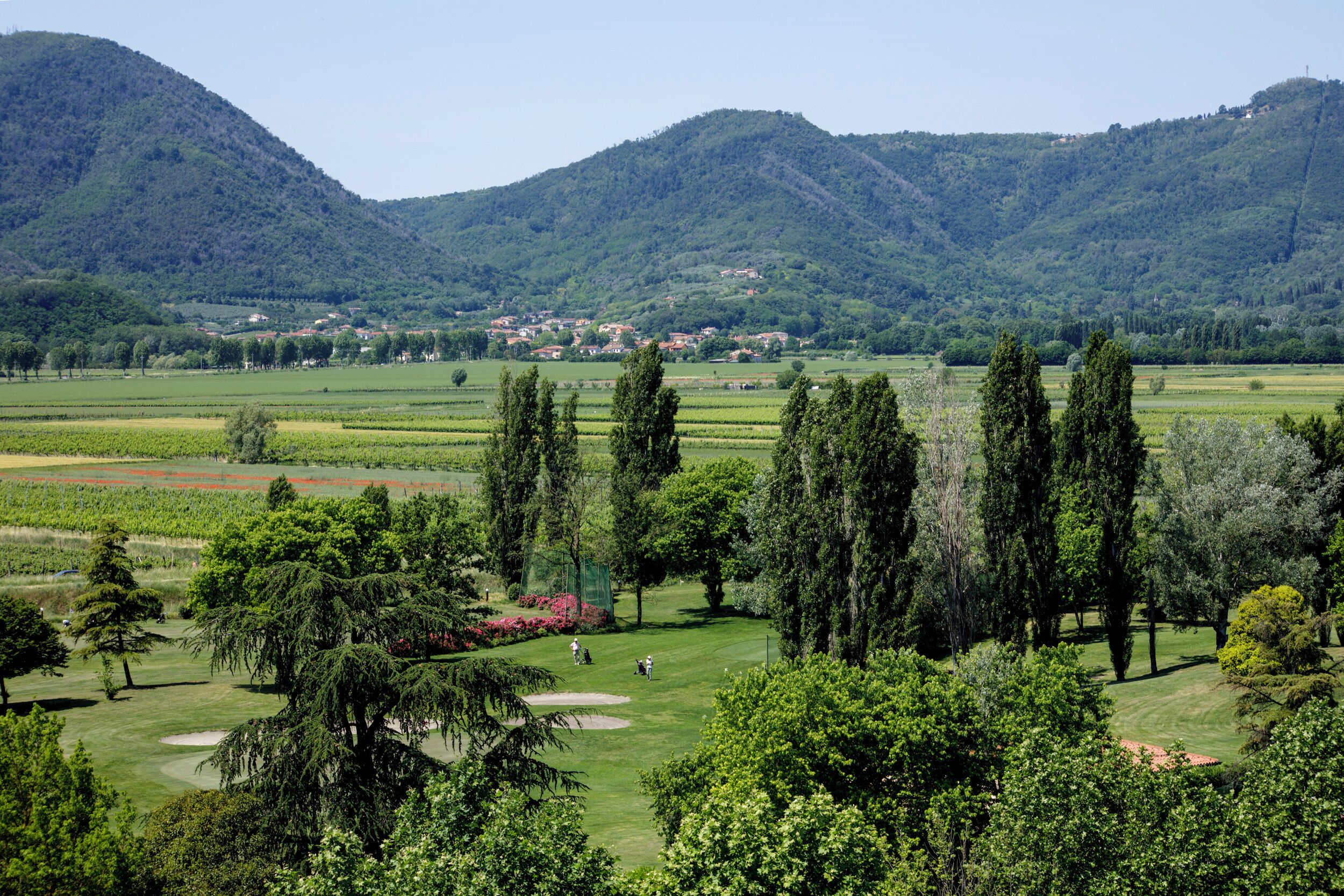 A golf course with a view of a town in the distance, surrounded by hills and trees.