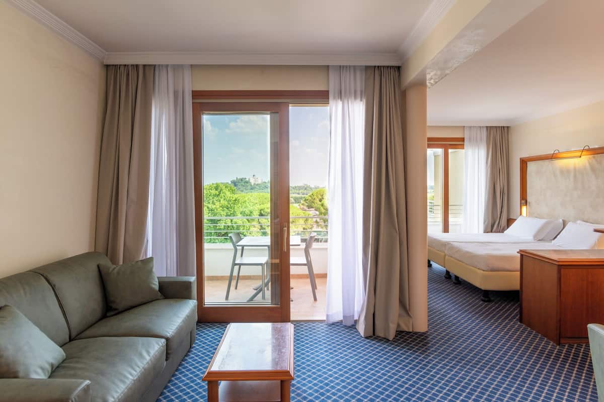Une chambre d’hôtel avec un canapé, un lit, une petite table et un balcon donnant sur un paysage verdoyant.