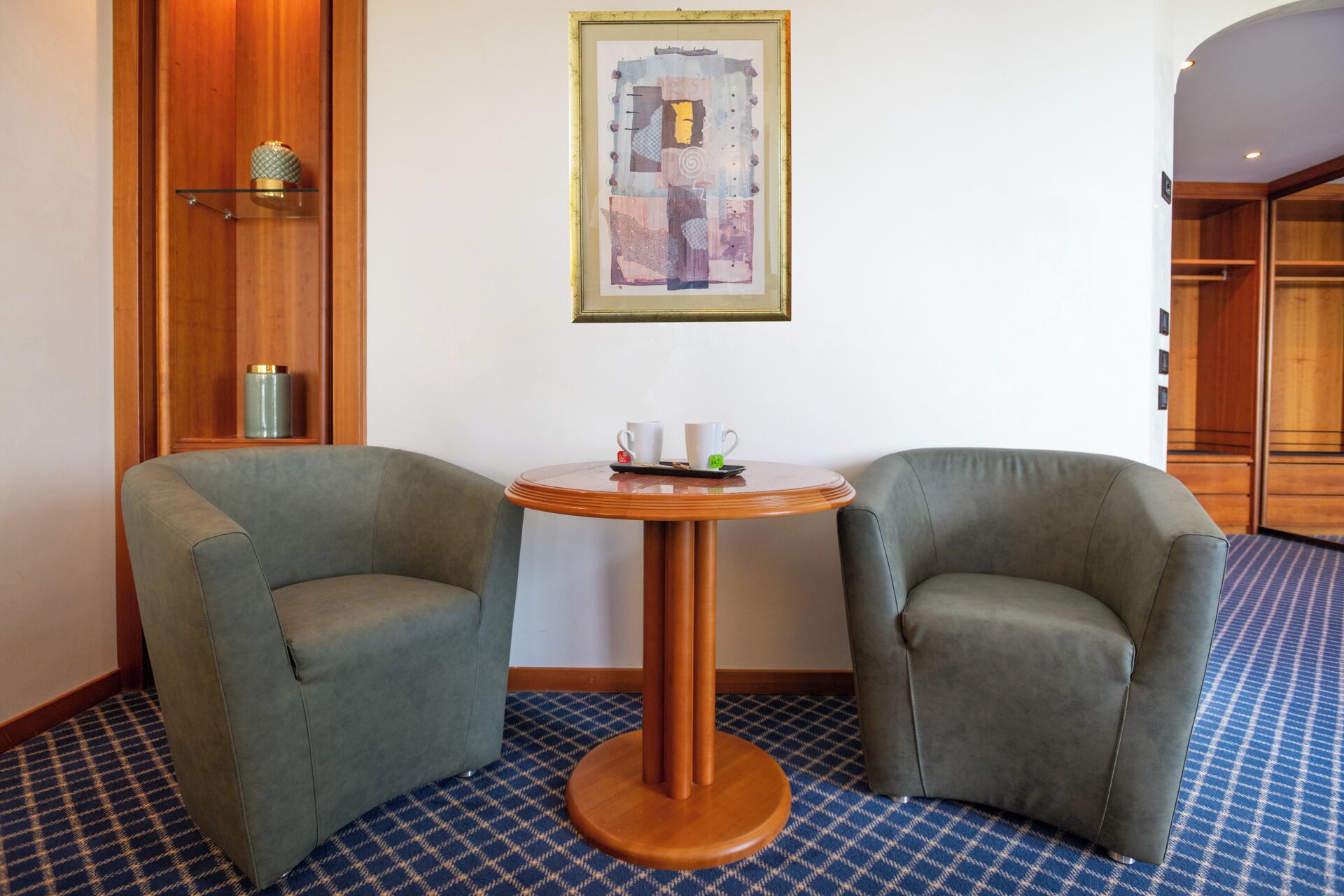 Una habitación de hotel con dos sillones, una mesa redonda de madera y un cuadro en la pared.