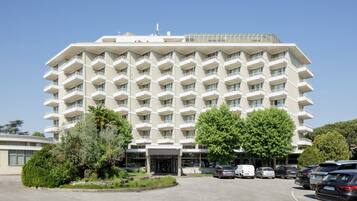 Un hotel de varios pisos con una fachada simétrica, una entrada central y un estacionamiento con varios automóviles.