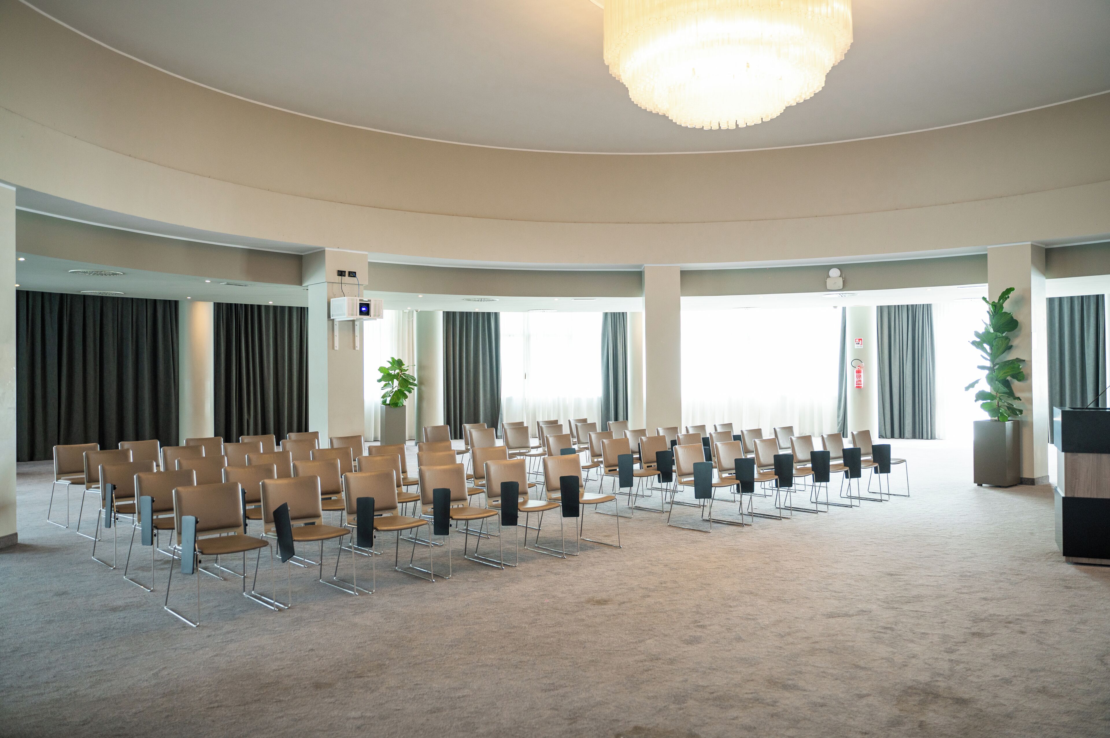 Ein Konferenzraum mit Stuhlreihen, großen Fenstern und einer Kristallleuchtre.'