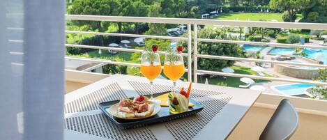 A balcony with a table set for two, overlooking a pool and lush greenery.