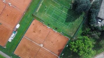 Vista aérea de un complejo deportivo con varias canchas de tenis, un estacionamiento y zonas verdes circundantes.