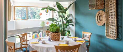 A dining area with a round table, four chairs, a potted plant, and decorative baskets on the wall.