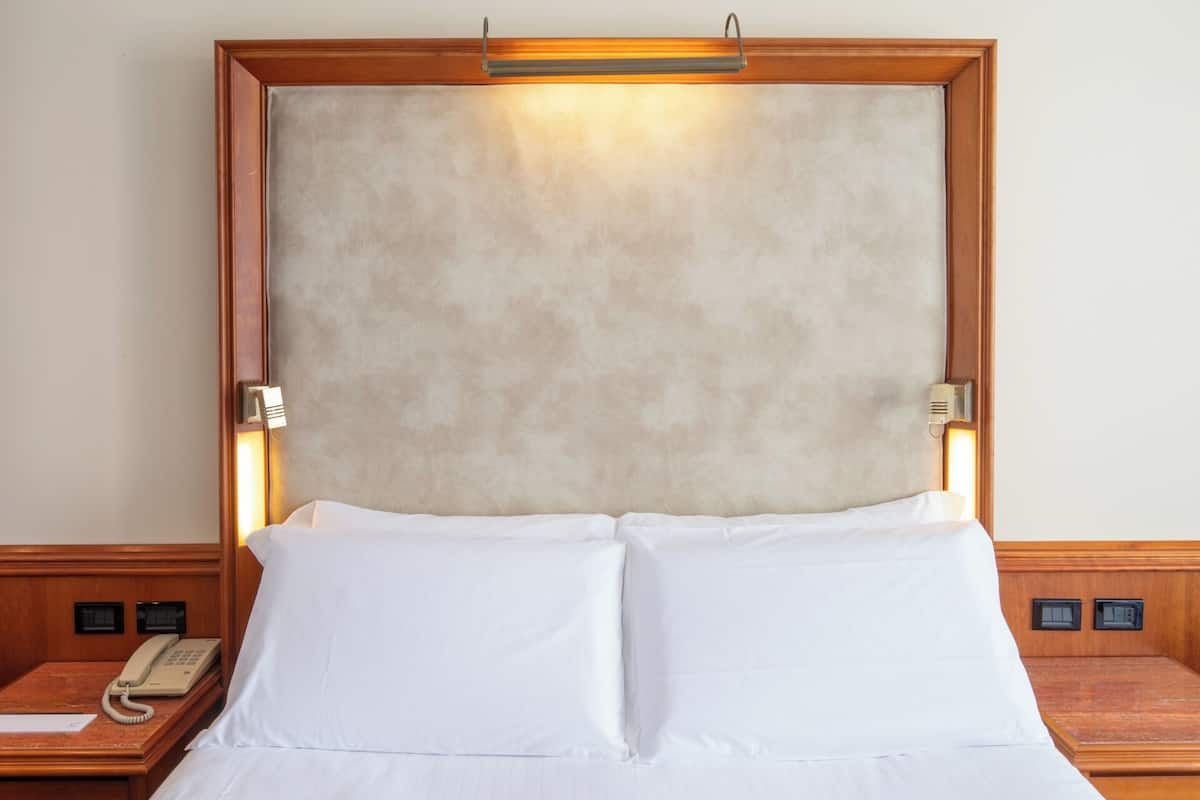Une chambre d’hôtel avec un grand lit, une tête de lit en bois, un téléphone sur la table de chevet et un luminaire fixé au mur.