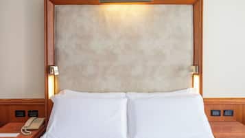 Una habitación de hotel con una cama grande, un cabecero de madera, un teléfono en la mesita de noche y una lámpara fijada a la pared.