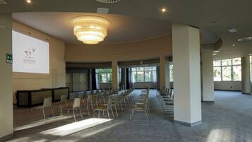 Una amplia sala de conferencias con filas de sillas, una pantalla grande y una araña.