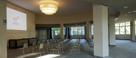 Une salle de conférence spacieuse, avec des rangées de chaises, un grand écran et un lustre.