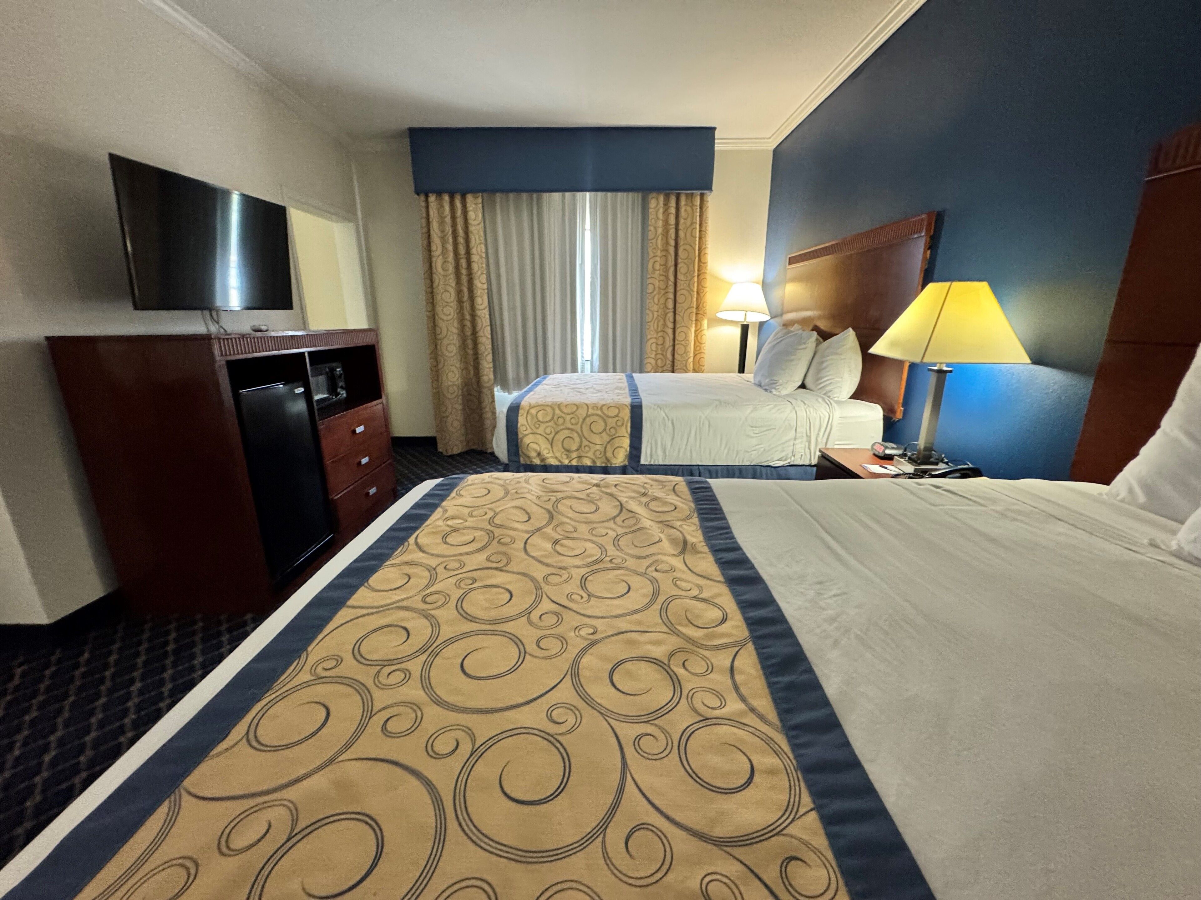 Habitación de hotel con dos camas, televisión, escritorio, lámpara y armario.