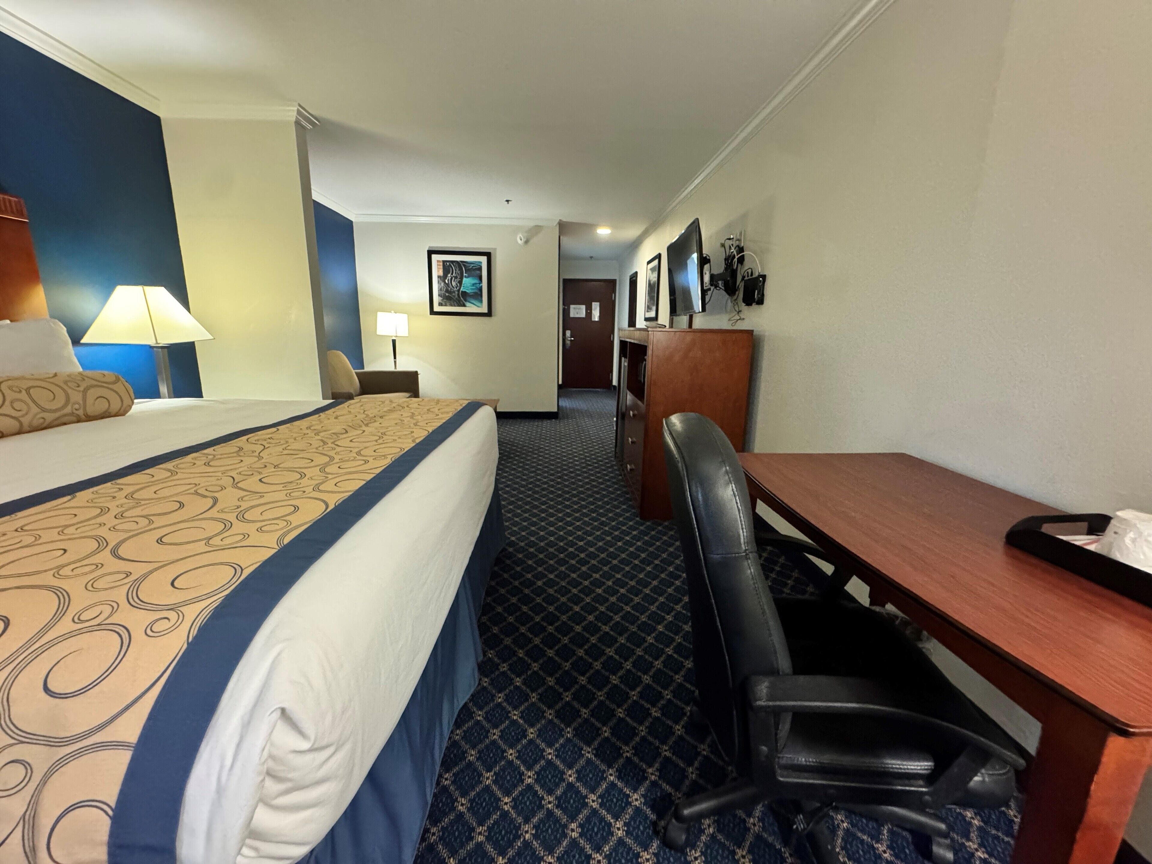 A hotel room with a bed, a desk, a chair, a lamp, and a picture on the wall.