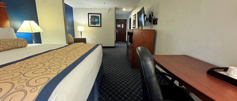A hotel room with a bed, a desk, a chair, a lamp, and a picture on the wall.