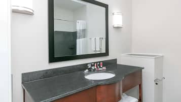 A bathroom with a granite countertop sink, a wooden vanity, a large mirror, and a towel rack.