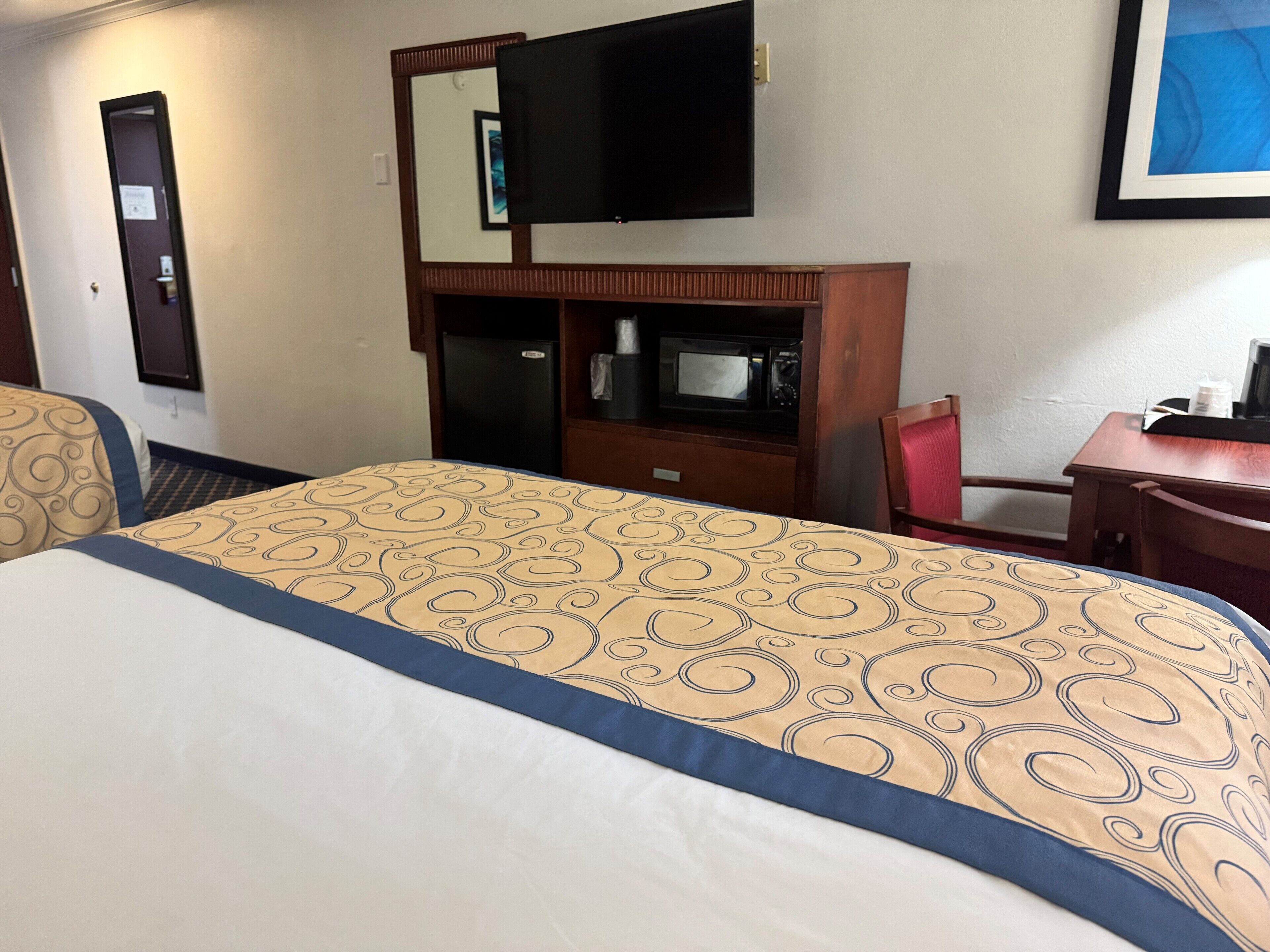 Quarto de hotel com cama, escrivaninha, cadeira, televisão, frigorífico e micro-ondas.