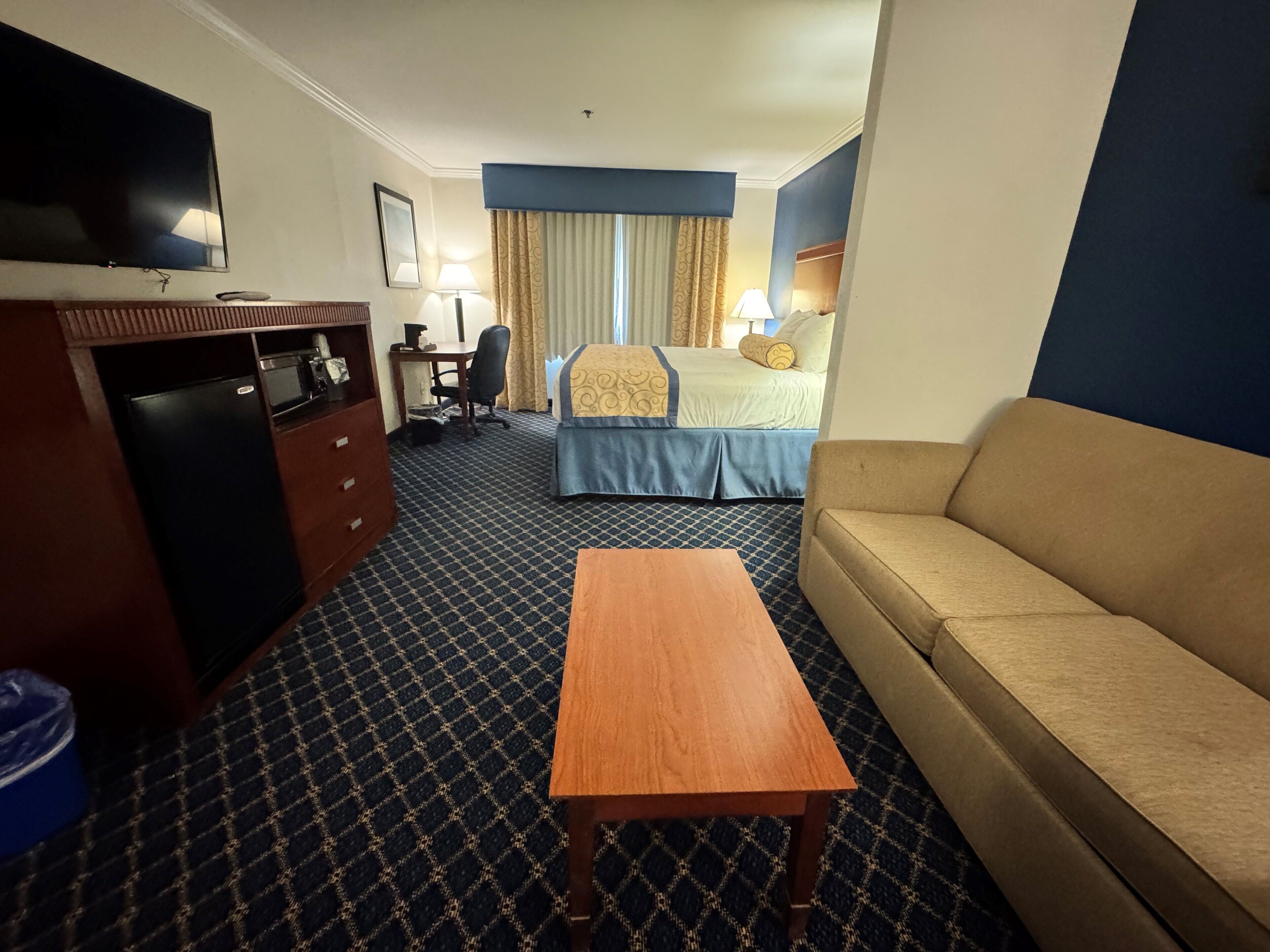 Una habitación de hotel con cama, sofá, escritorio, televisor y una pequeña mesa.