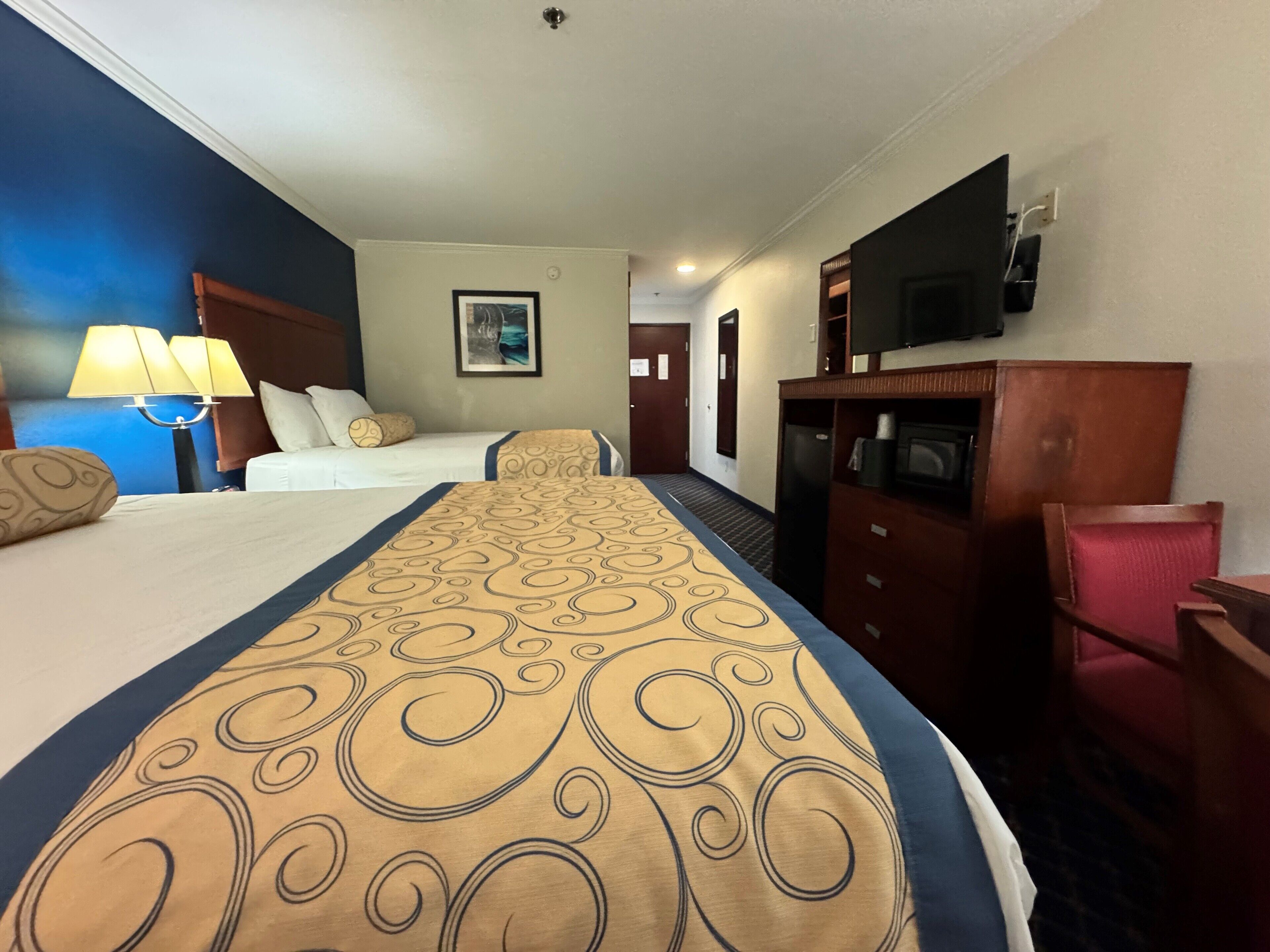 A hotel room with two beds, a television, a desk, and a chair.