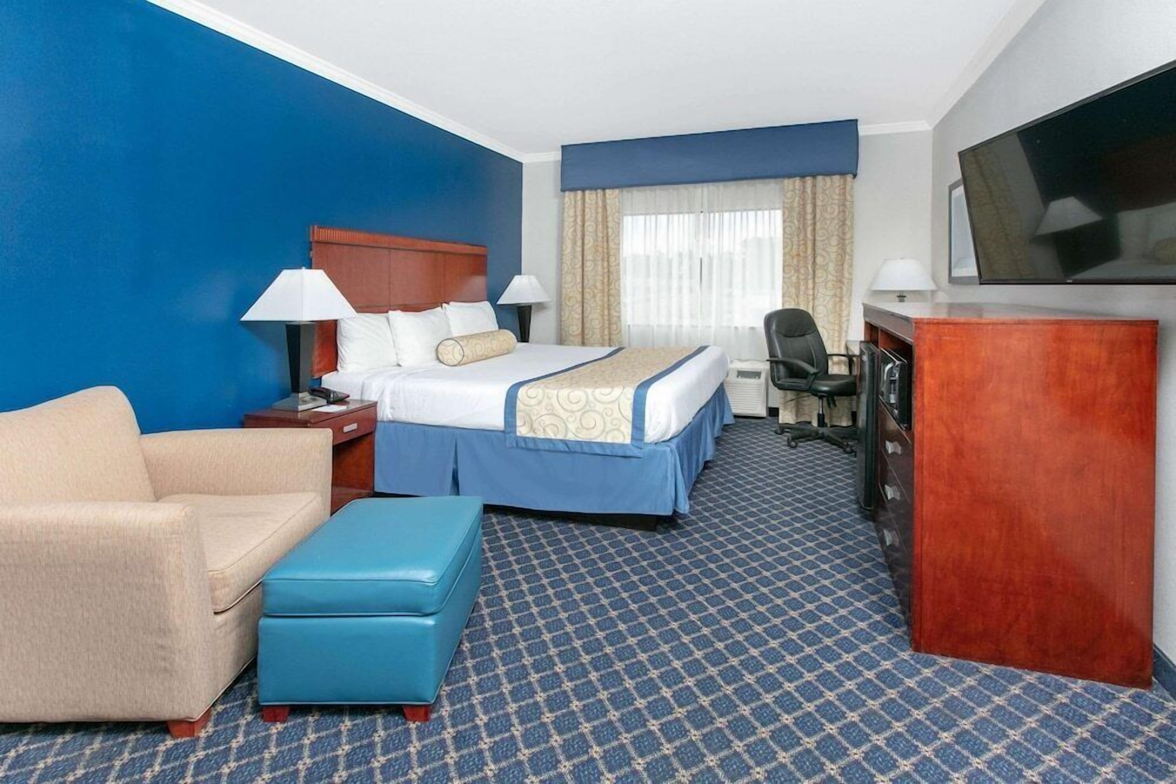 Quarto de hotel com cama, escrivaninha, televisão, sofá e tapete estampado.