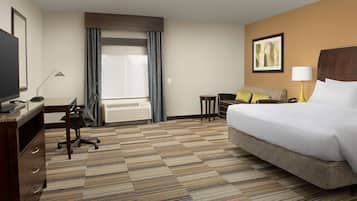 A hotel room with a large bed, a desk with a chair, a television, and a window with curtains.