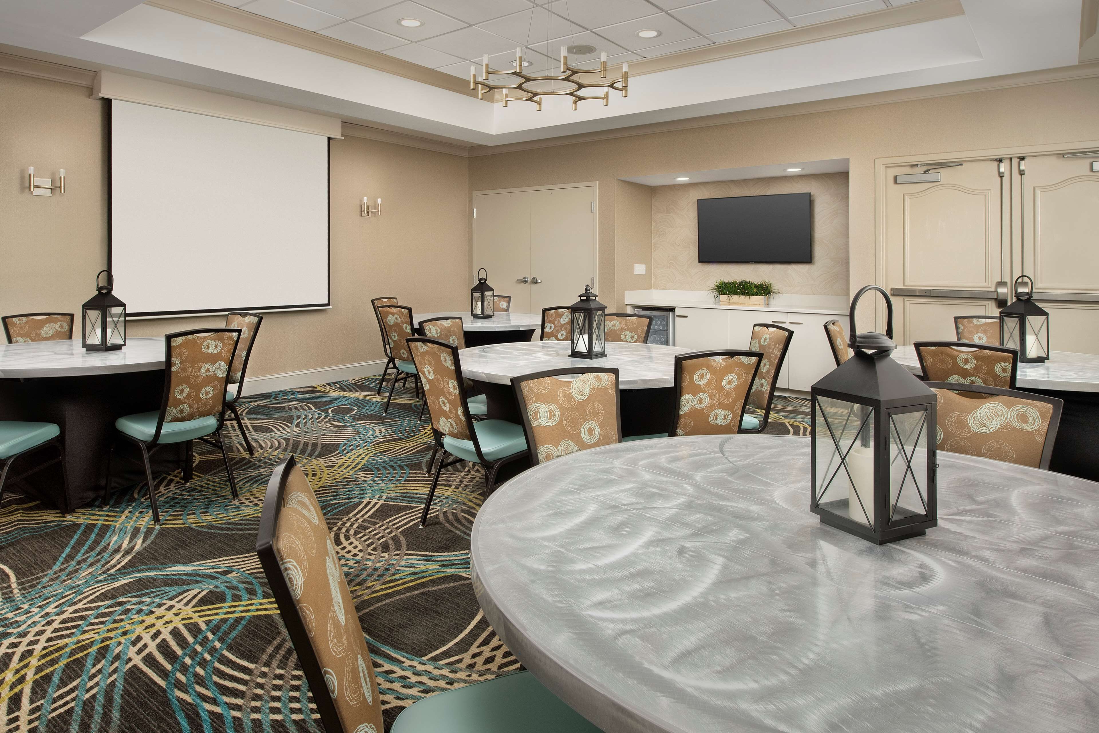 A conference room with a large table, chairs, a projector screen, and a television.