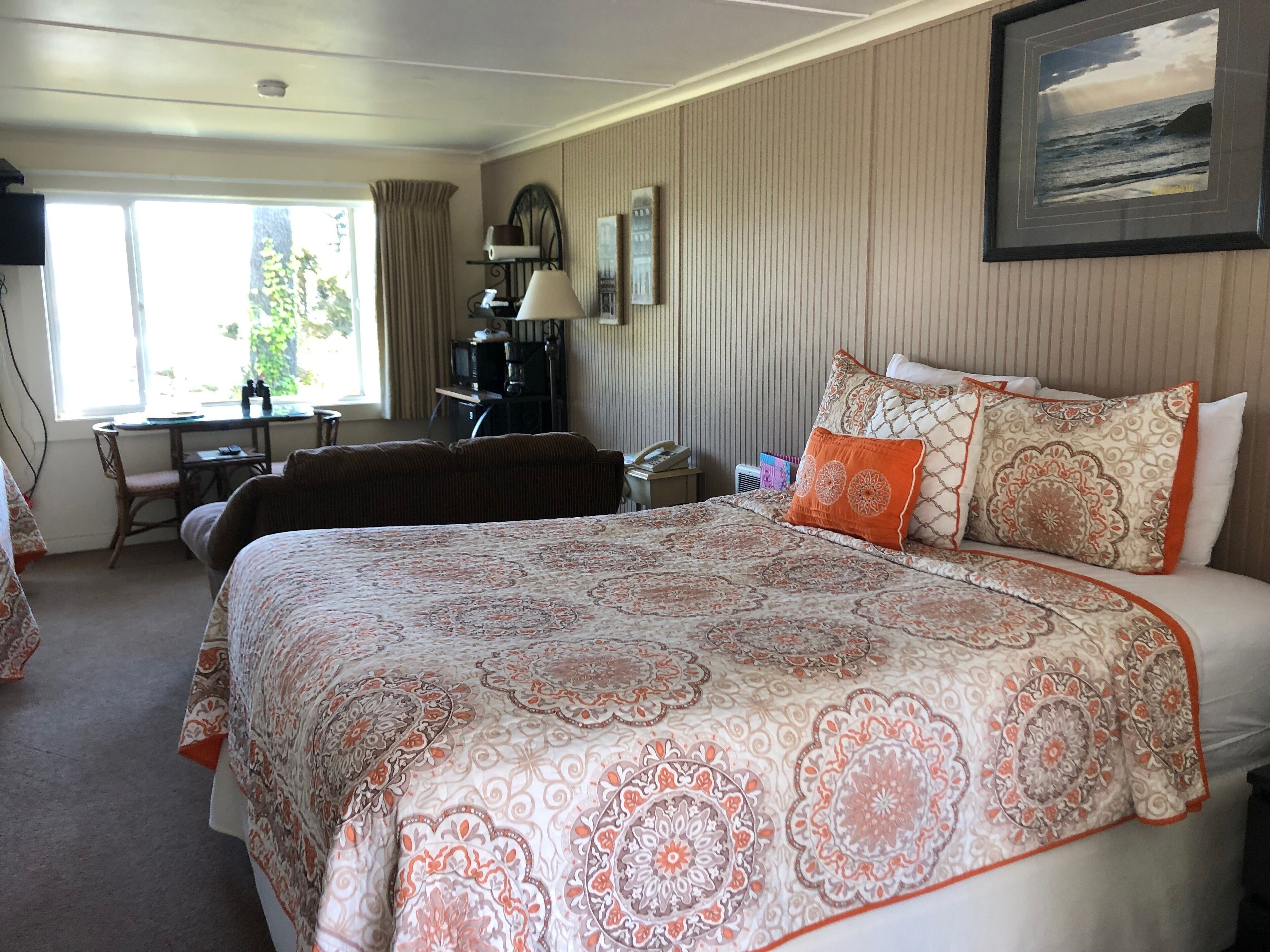 A hotel room with a large bed, a desk with a chair, a telephone, and a window with curtains.