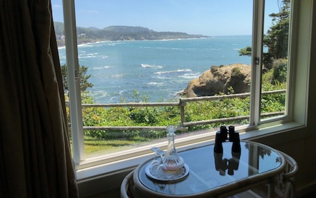 A room with a large window offering a view of the ocean and cliffs.