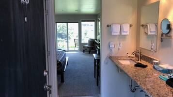 A hotel room with a large window, a bed, a seating area, a bathroom with a sink and mirror, and a door marked with the number 16.