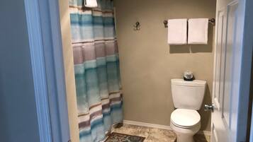 Un baño con cortina de ducha a rayas, un inodoro, un felpudo estampado y dos toallas colgadas en la pared.