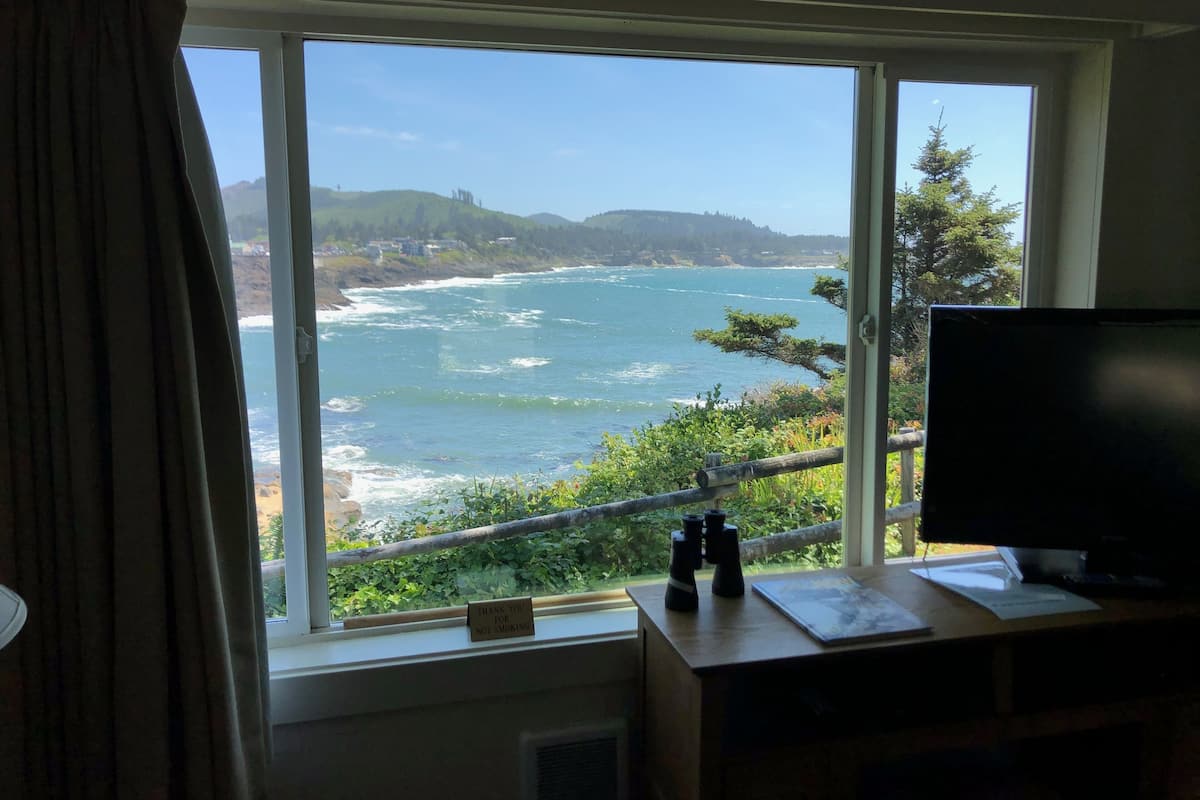 A room with a large window overlooking a coastal view, a desk with binoculars, and a "Thank you for not smoking" sign.