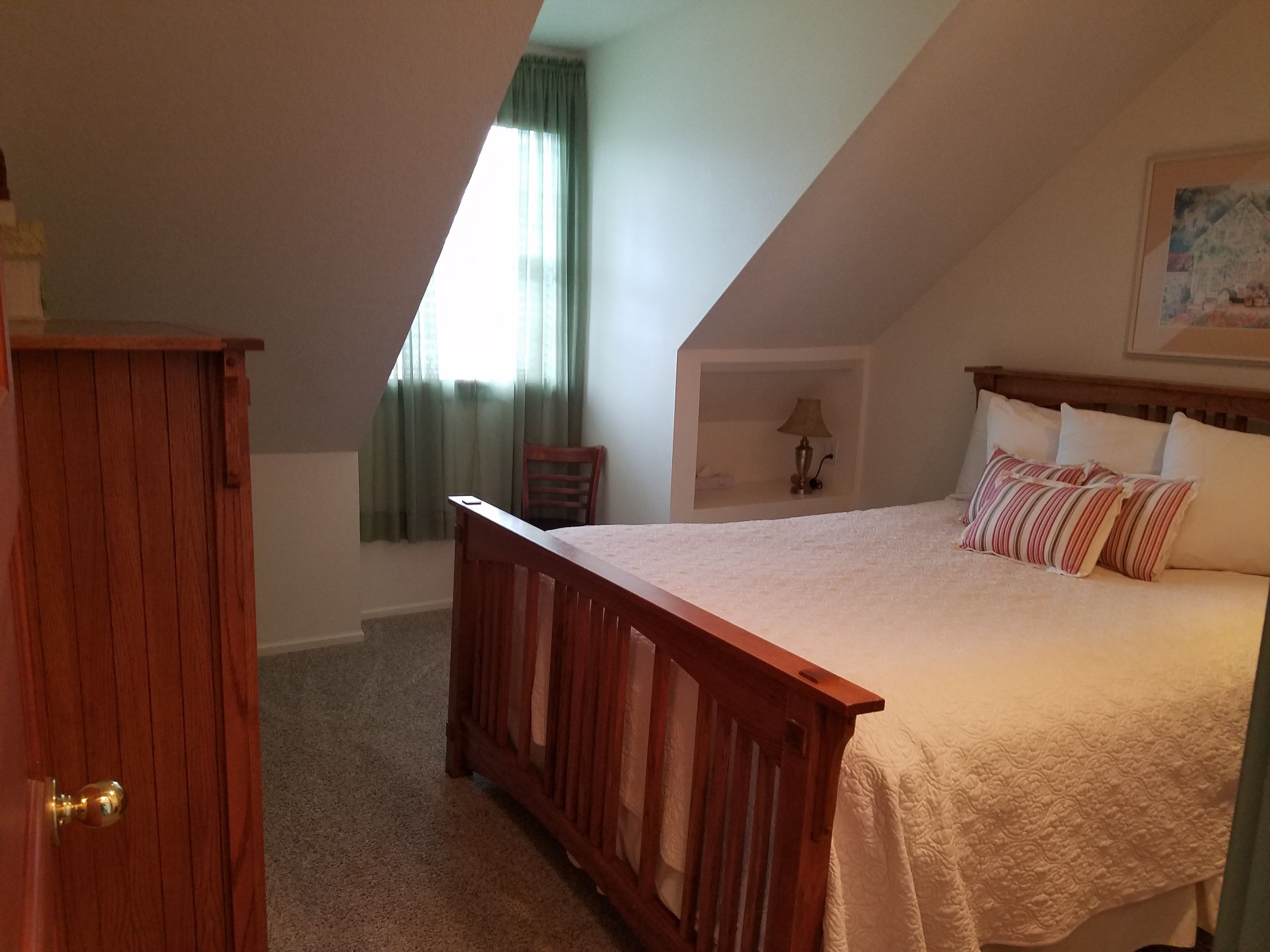 A bedroom with a wooden bed, a nightstand, a lamp, and a window with curtains.