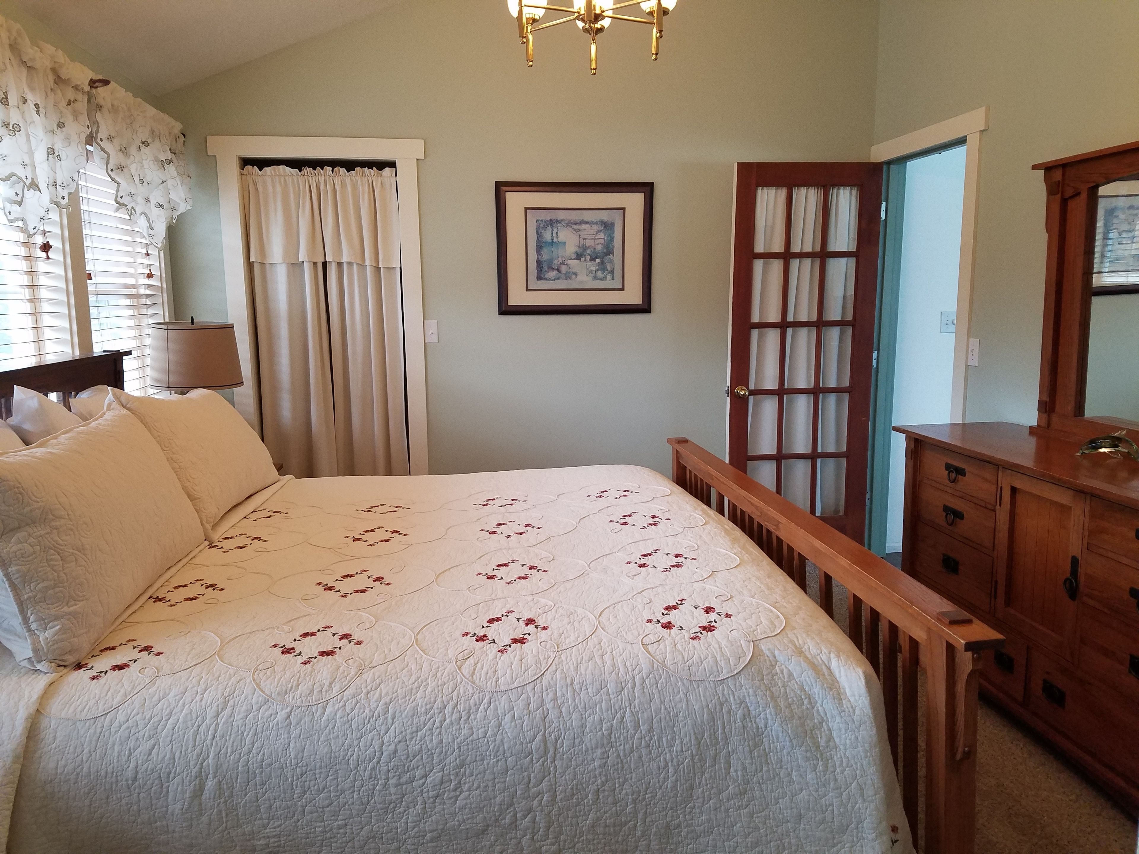 A bedroom with a bed, a wooden dresser, a framed picture on the wall, and a door with glass panels.