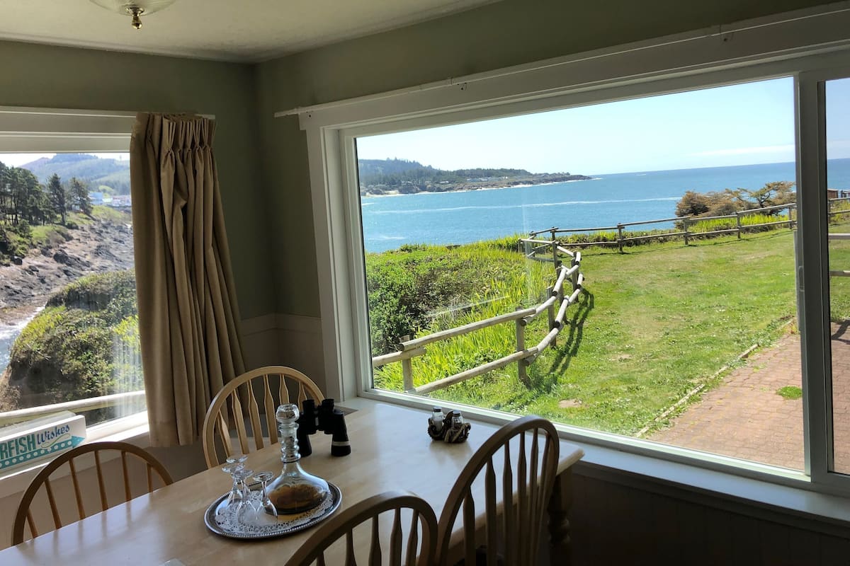 A dining area with a table, chairs, and a view of the sea and hills.