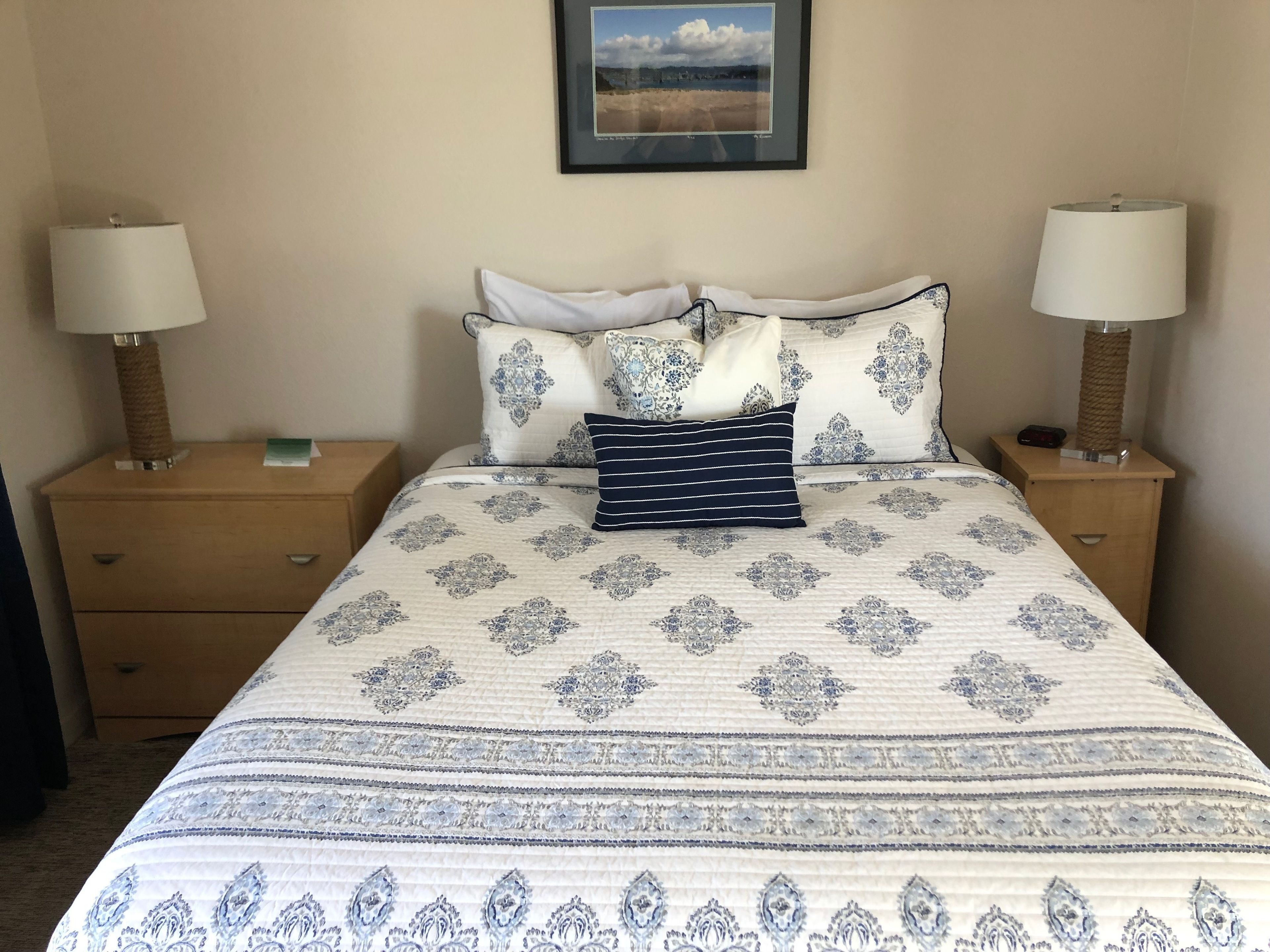 A neatly made bed with a patterned bedspread, two bedside tables with lamps, and a framed picture on the wall.