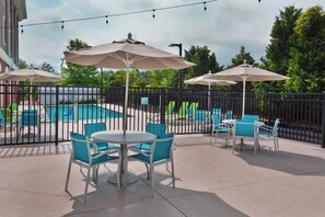 A poolside area with a fenced pool, lounge chairs, and umbrellas.