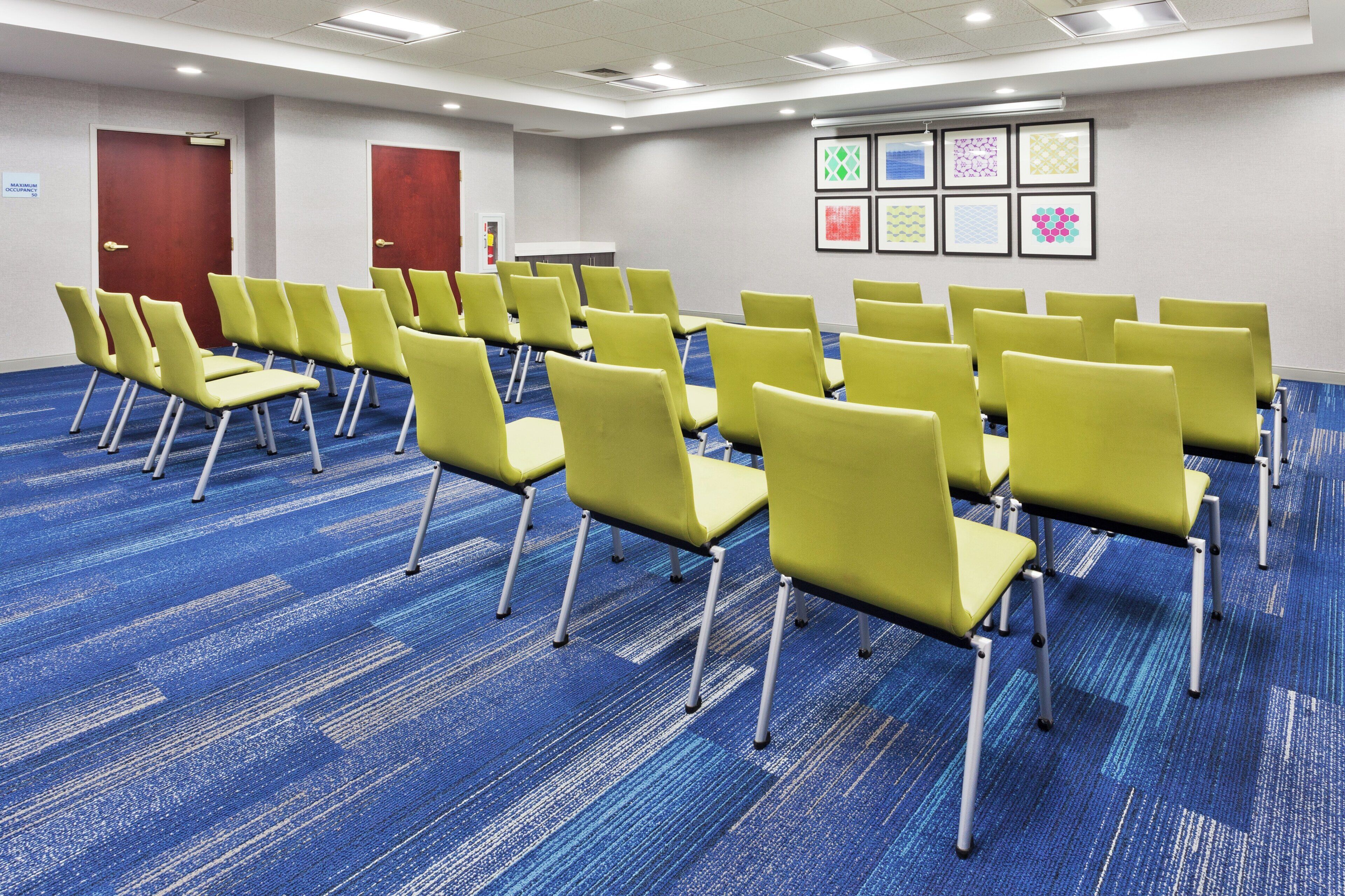 A conference room with rows of yellow chairs, blue carpeting, and framed artwork on the wall.