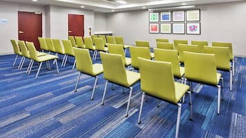 A conference room with rows of yellow chairs, blue carpeting, and framed artwork on the wall.