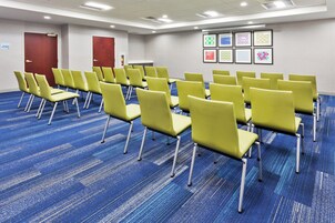 Un salón de conferencias con hileras de sillas amarillas, alfombra azul y obras de arte enmarcadas en la pared.
