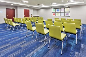 A conference room with rows of yellow chairs, blue carpeting, and framed artwork on the wall.