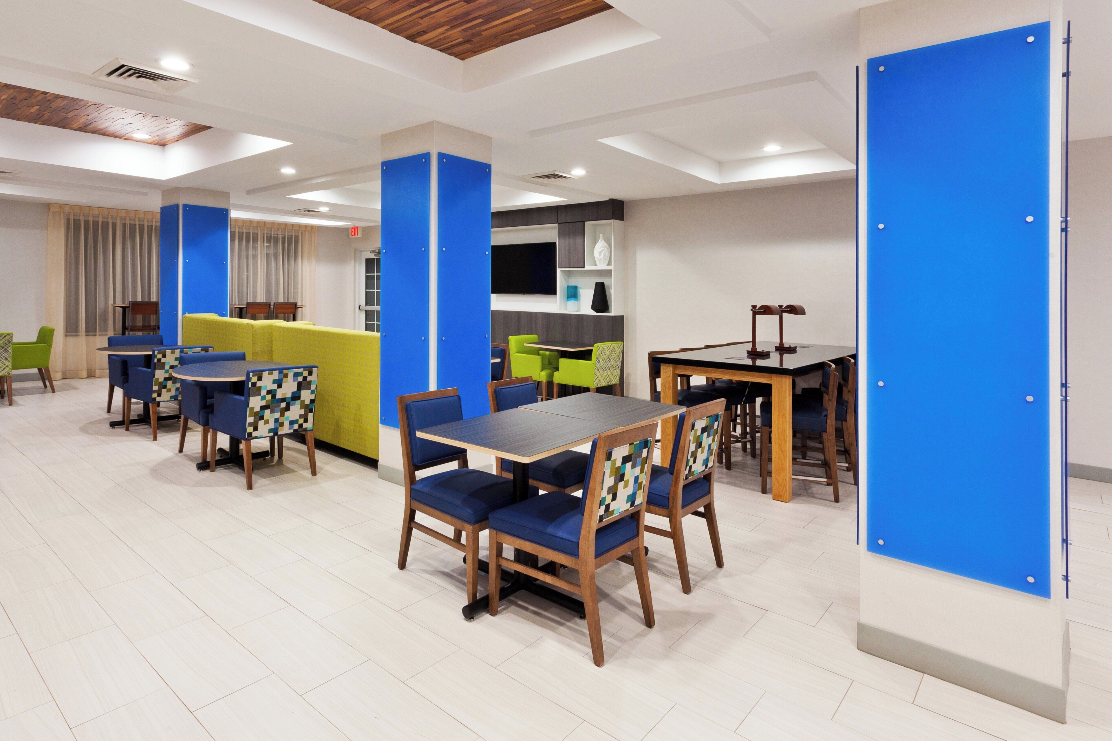 A modern dining area with wooden tables and chairs, a sofa, and a blue accent wall.
