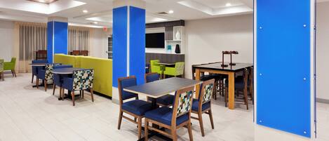 A modern dining area with wooden tables and chairs, a sofa, and a blue accent wall.