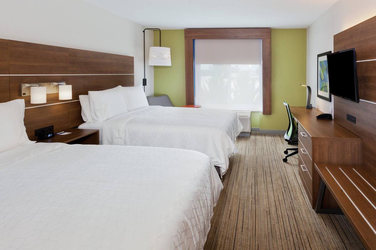 Habitación de hotel con dos camas, un escritorio, una silla, un televisor y una ventana con persianas.