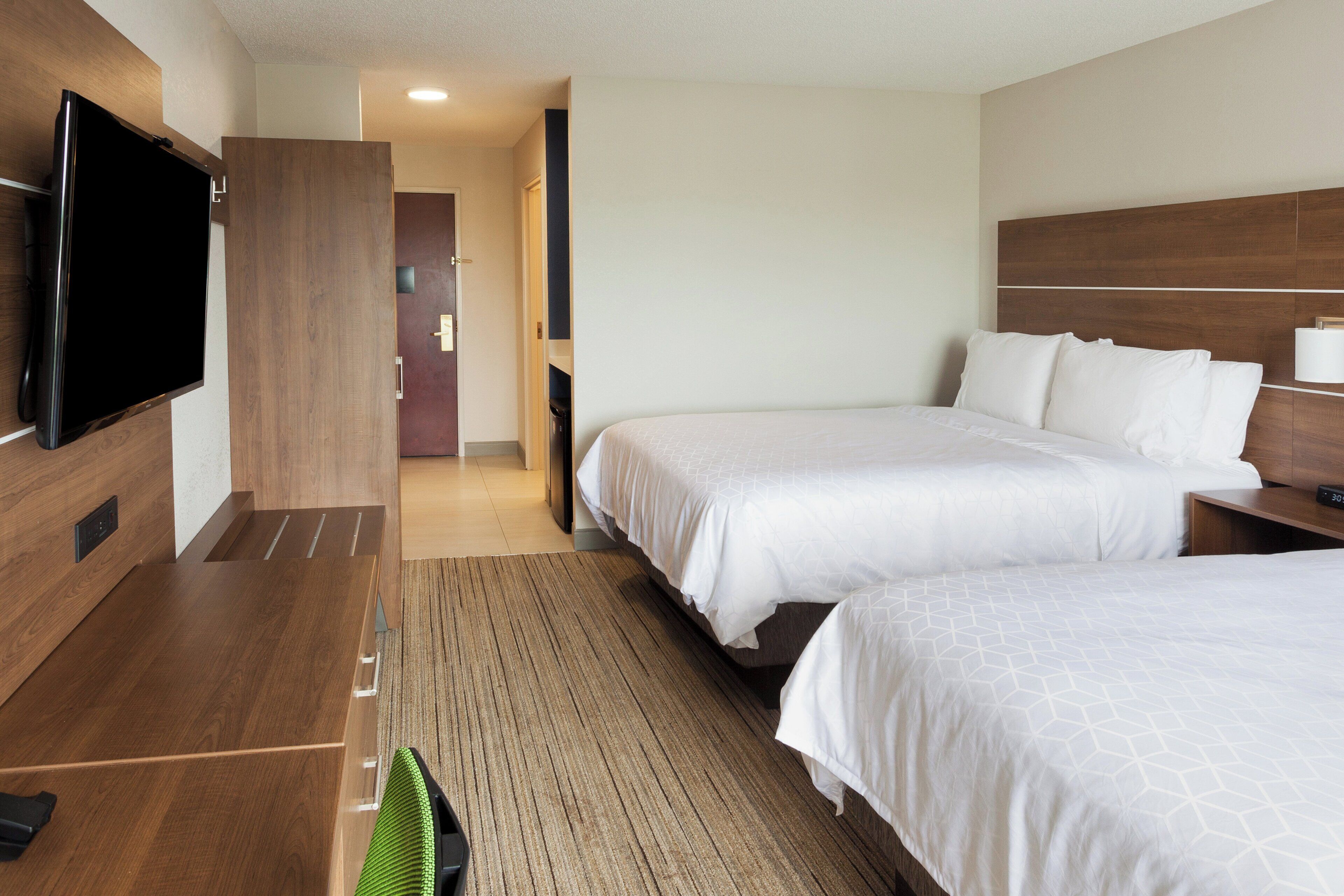 Ein Hotelzimmer mit zwei Betten, einem Flachbildfernseher, einem Holztisch und einem modernen Design.