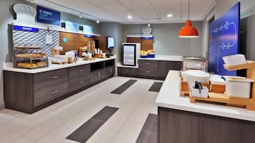A breakfast area with a bakery display, cereal, and fruit options.